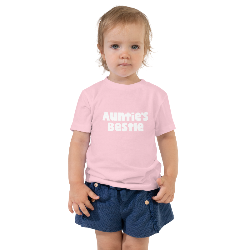 A child wearing a pink t-shirt with white text on the front that reads 'Auntie's Bestie. By Less Hustle, More Joy.