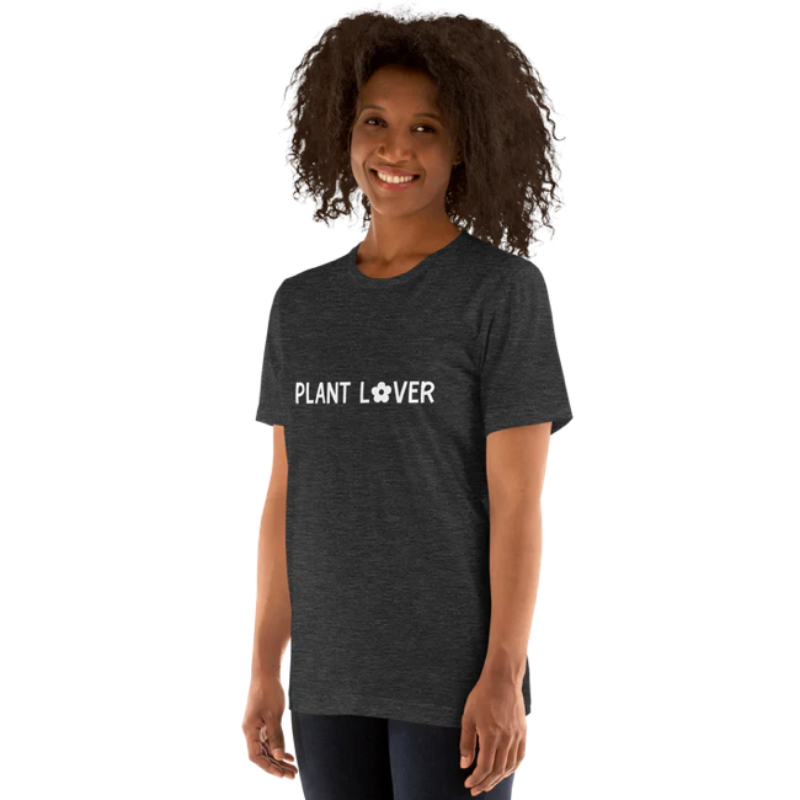 A person shown from the side wearing a dark grey heather t-shirt by Less Hustle, More Joy, with the words 'PLANT LOVER' printed on the front in white text.