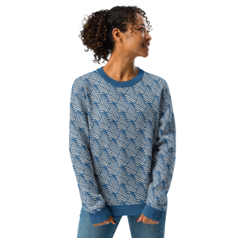 A person wearing a crew-neck knitted sweater with a wave pattern in blue and sand colours by Less Hustle, More Joy.