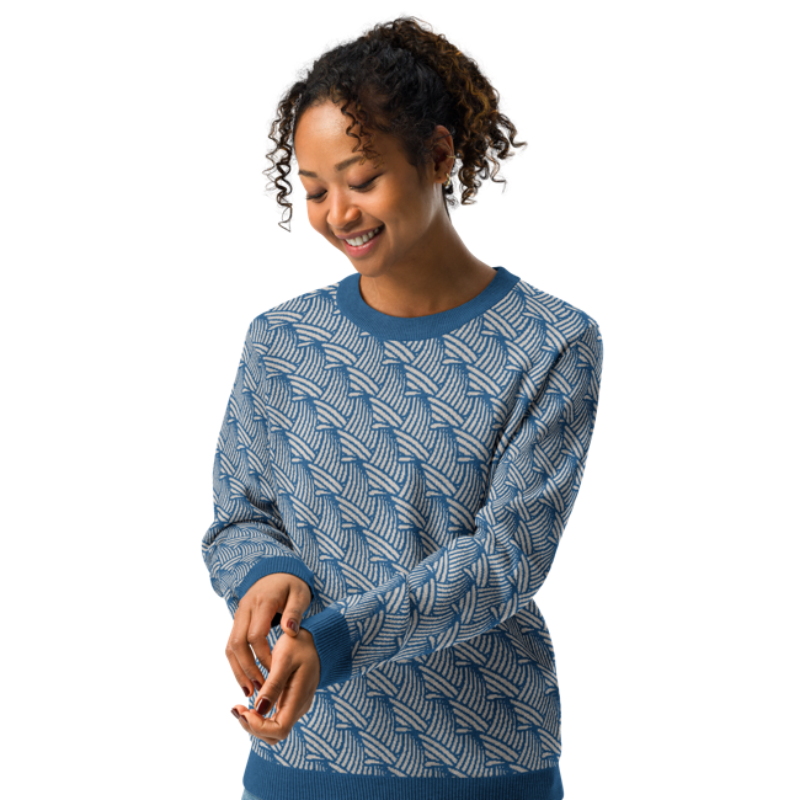 A person wearing a crew-neck knitted sweater with a wave pattern in blue and sand colours by Less Hustle, More Joy.