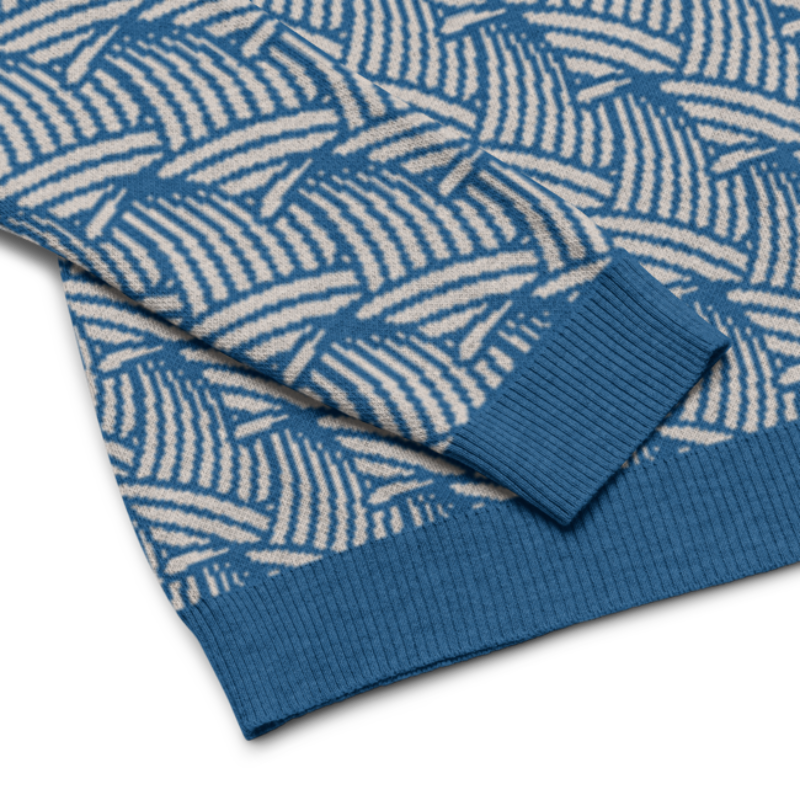 Detail image of the sleeve and bottom hem of a crew-neck knitted sweater with a wave pattern in blue and sand colours by Less Hustle, More Joy.