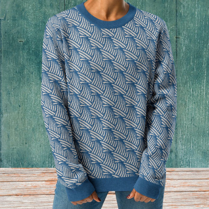 A person wearing a crew-neck knitted sweater with a wave pattern in blue and sand colours by Less Hustle, More Joy.