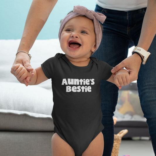 Baby wearing a black onesie with 'Auntie's Bestie' text, learning to walk.