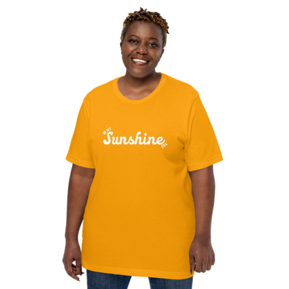 A person shown wearing a gold crew neck t-shirt by Less Hustle, More Joy with the phrase 'In My Sunshine Era' printed in white text on the front.