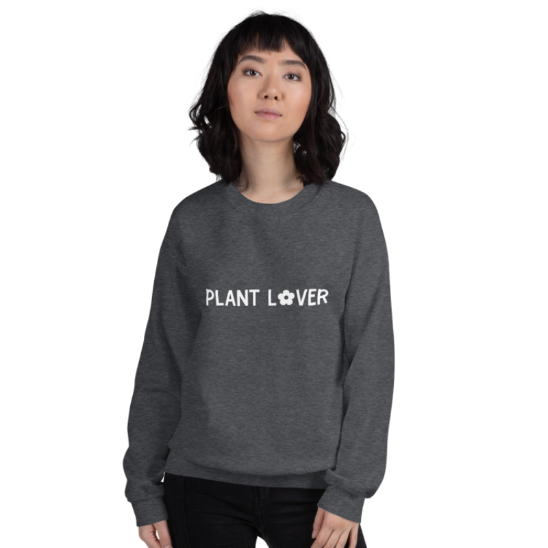 A person wearing a dark grey heather sweatshirt from Less Hustle, More Joy with the text 'PLANT LOVER' on the front in white.