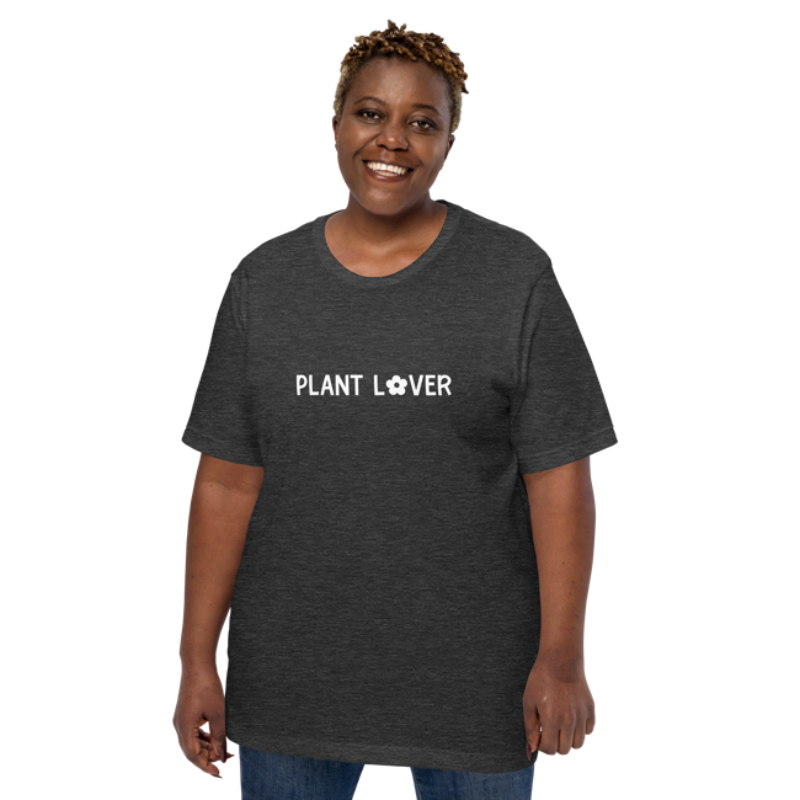 A person wearing a dark grey heather t-shirt by Less Hustle, More Joy, with the words 'PLANT LOVER' printed on the front in white text.