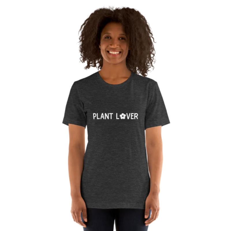 A person wearing a dark grey heather t-shirt by Less Hustle, More Joy, with the words 'PLANT LOVER' printed on the front in white text.