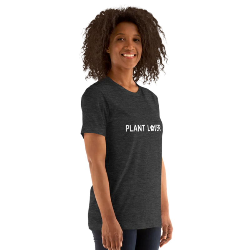 A person shown from the side wearing a dark grey heather t-shirt by Less Hustle, More Joy, with the words 'PLANT LOVER' printed on the front in white text.