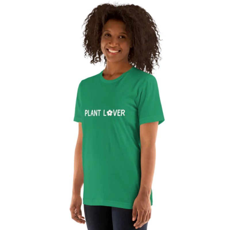 A person standing side-on wearing a kelly green heather t-shirt by Less Hustle, More Joy, with the words 'PLANT LOVER' printed on the front in white text.