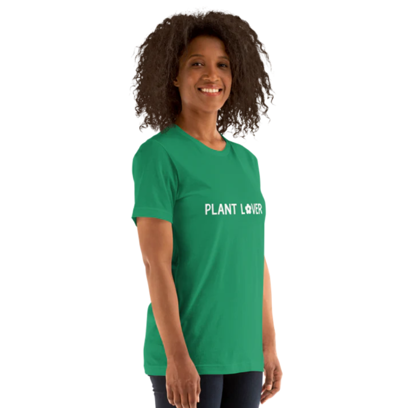 A person standing side-on wearing a kelly green heather t-shirt, by Less Hustle, More Joy, with the words 'PLANT LOVER' printed on the front in white text.