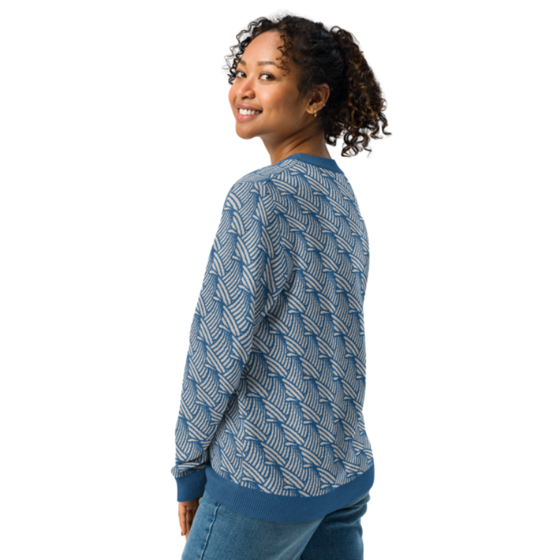 A person wearing a crew-neck knitted sweater with a wave pattern in blue and sand colours, turned side-on to show the back of the sweater by Less Hustle, More Joy.