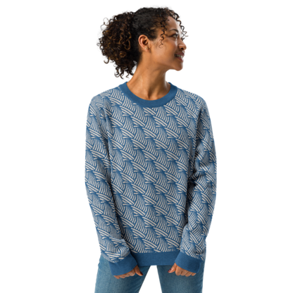 A person wearing a crew-neck knitted sweater with a wave pattern in blue and sand colours by Less Hustle, More Joy.
