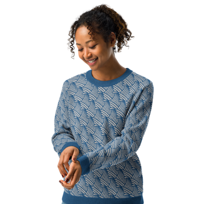 A person wearing a crew-neck knitted sweater with a wave pattern in blue and sand colours by Less Hustle, More Joy.